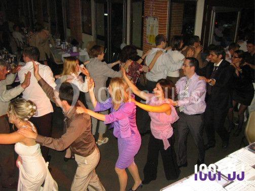 Des personnes en tenue de soirée dansent en file indienne dans une salle de réception.