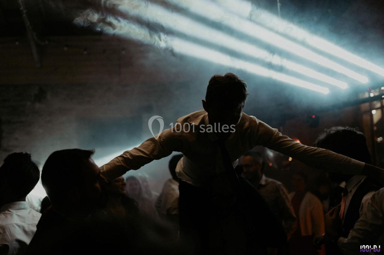 Un homme en chemise blanche est porté par une foule dans une ambiance sombre avec des lumières vives en arrière-plan.