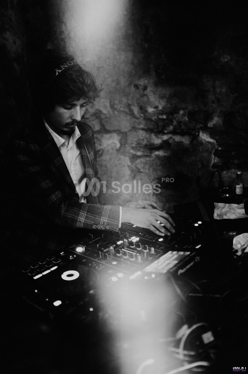 Un DJ mixant de la musique sur une table de mixage dans une ambiance sombre et tamisée.