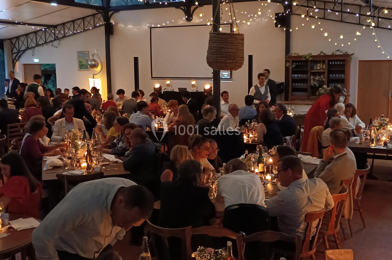 Salle remplie de convives dînant à des tables décorées de bougies, dans une ambiance chaleureuse et festive.