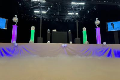 Salle de réception avec scène éclairée par des projecteurs orange, décorée de ballons suspendus.