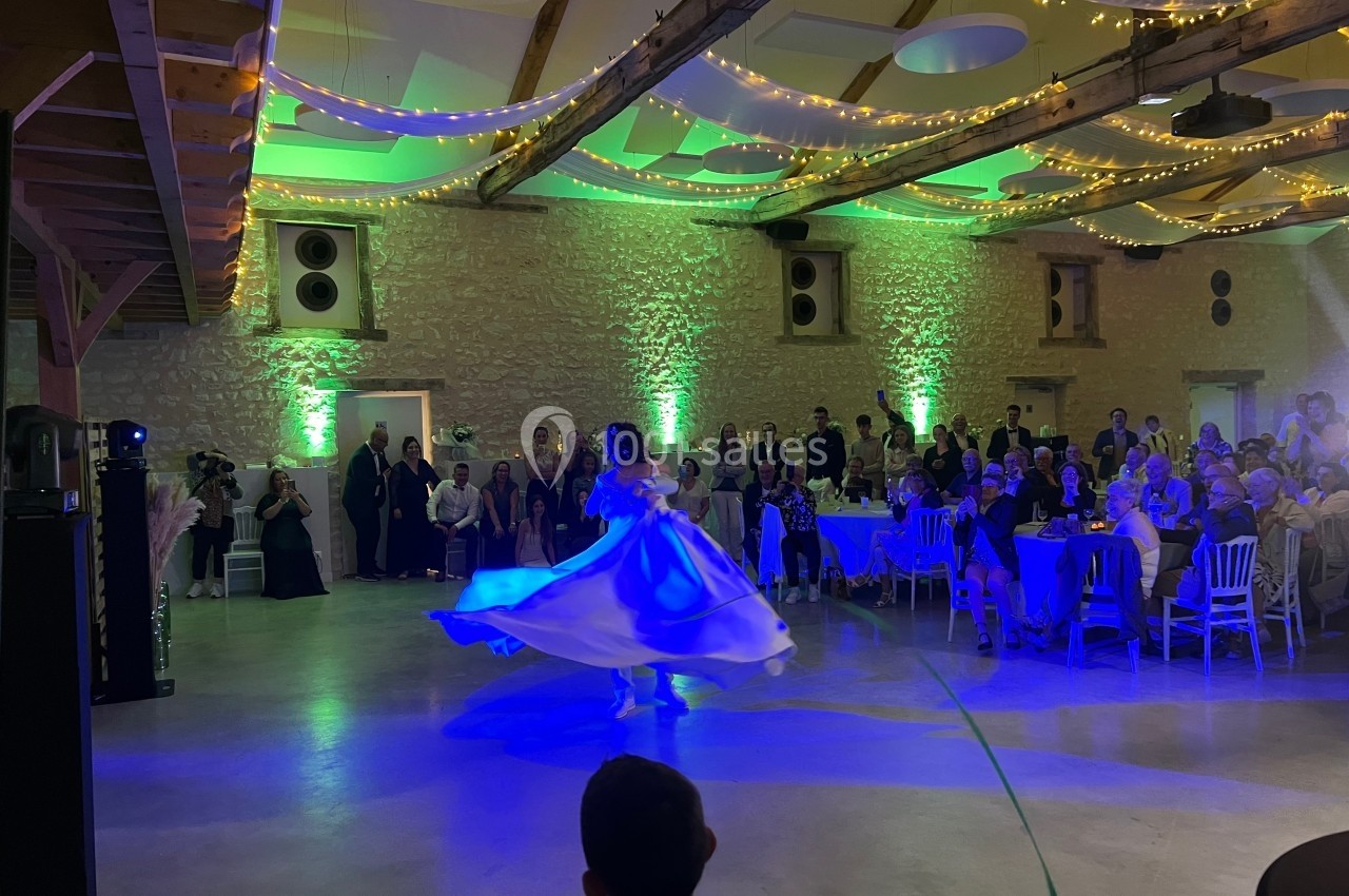 Une mariée danse dans une salle de réception éclairée de guirlandes lumineuses, entourée d'invités assis et debout.