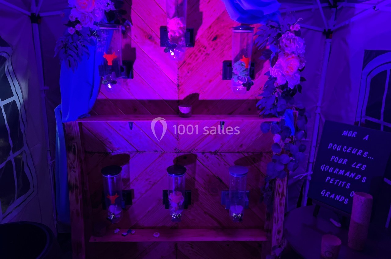 Mur de distributeurs de bonbons éclairé par une lumière violette, décoré de fleurs et d'un panneau écrit à la main.