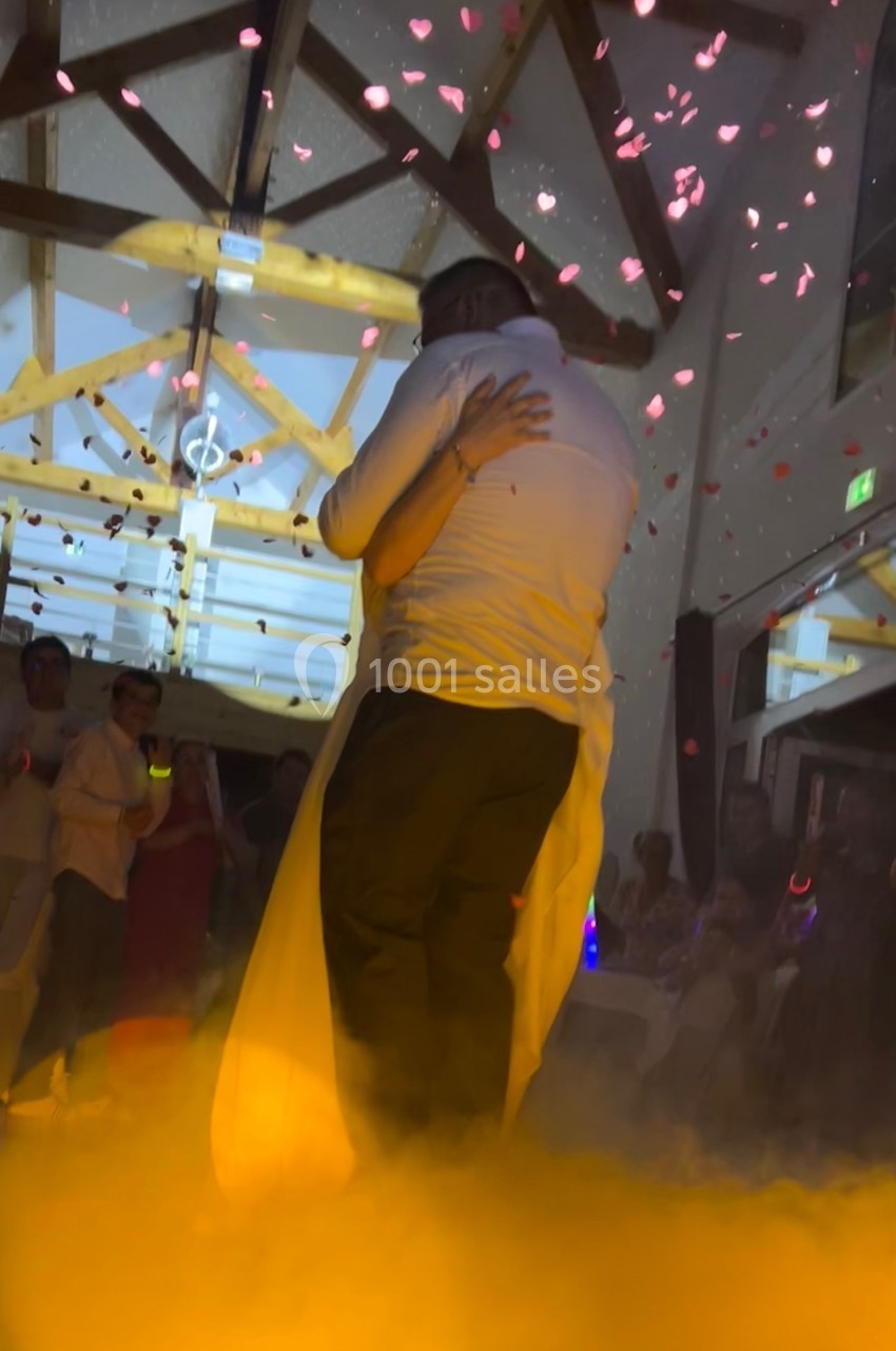 Un couple s'enlace sur une piste de danse entourée de fumée et de pétales, sous un éclairage tamisé.