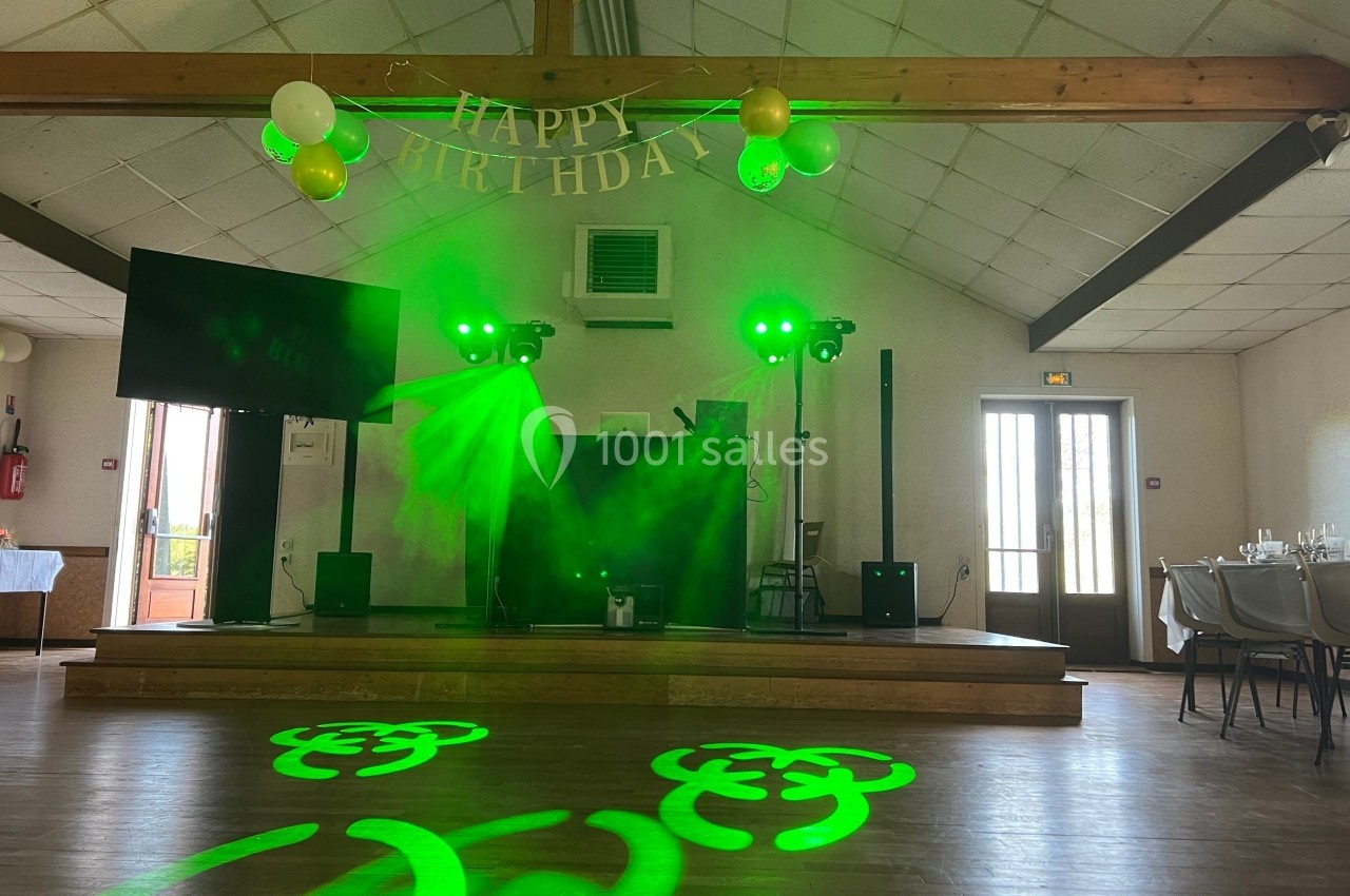 Salle décorée pour un anniversaire avec éclairage vert, guirlande ’Happy Birthday’ et tables dressées en arrière-plan.