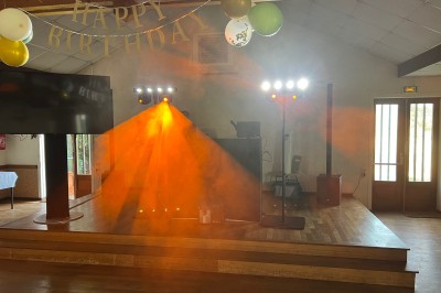 Salle de réception avec scène éclairée par des projecteurs orange, décorée de ballons suspendus.