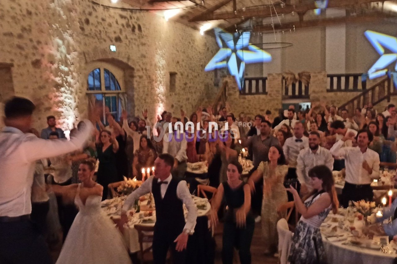 Des invités dansent et célèbrent dans une grande salle en pierre décorée de lumières et d'étoiles suspendues.