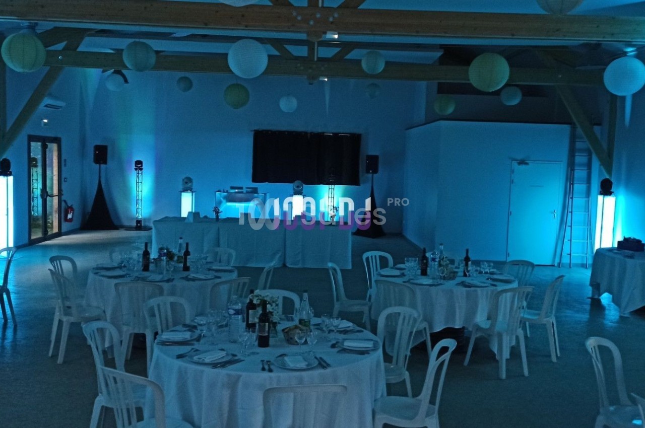 Salle de réception décorée avec des tables rondes dressées, éclairage bleu et éléments suspendus au plafond.