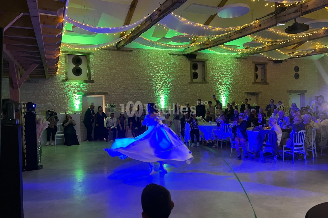 Une mariée danse dans une salle de réception éclairée de guirlandes lumineuses, entourée d'invités assis et debout.