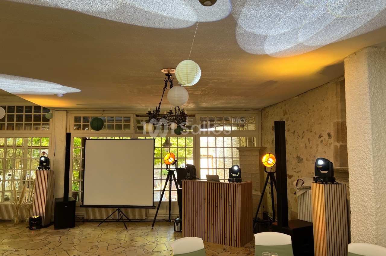 Salle de réception avec projecteurs, écran de projection, tables dressées et décorations lumineuses au plafond.