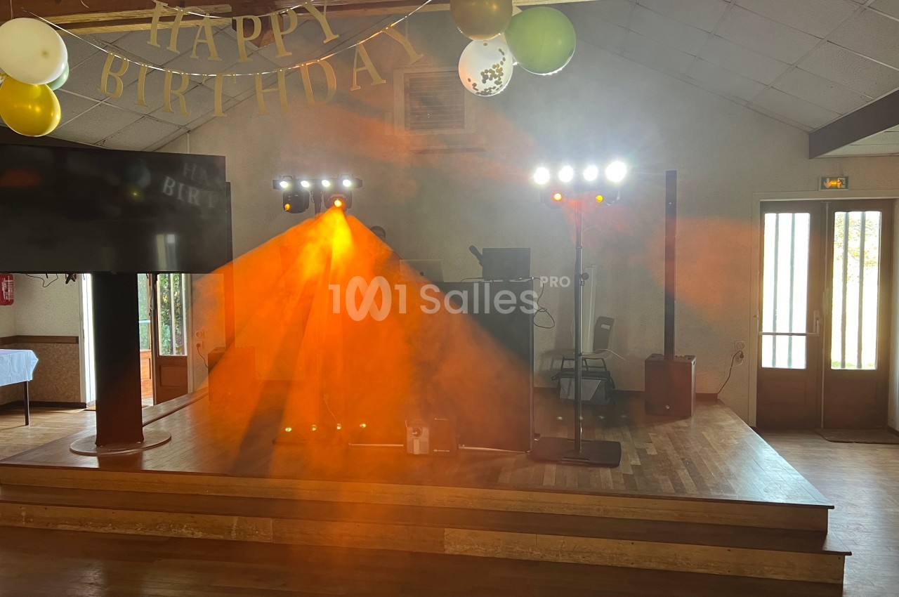Scène décorée pour un anniversaire avec guirlande ’Happy Birthday’, jeux de lumière et fumée orange.