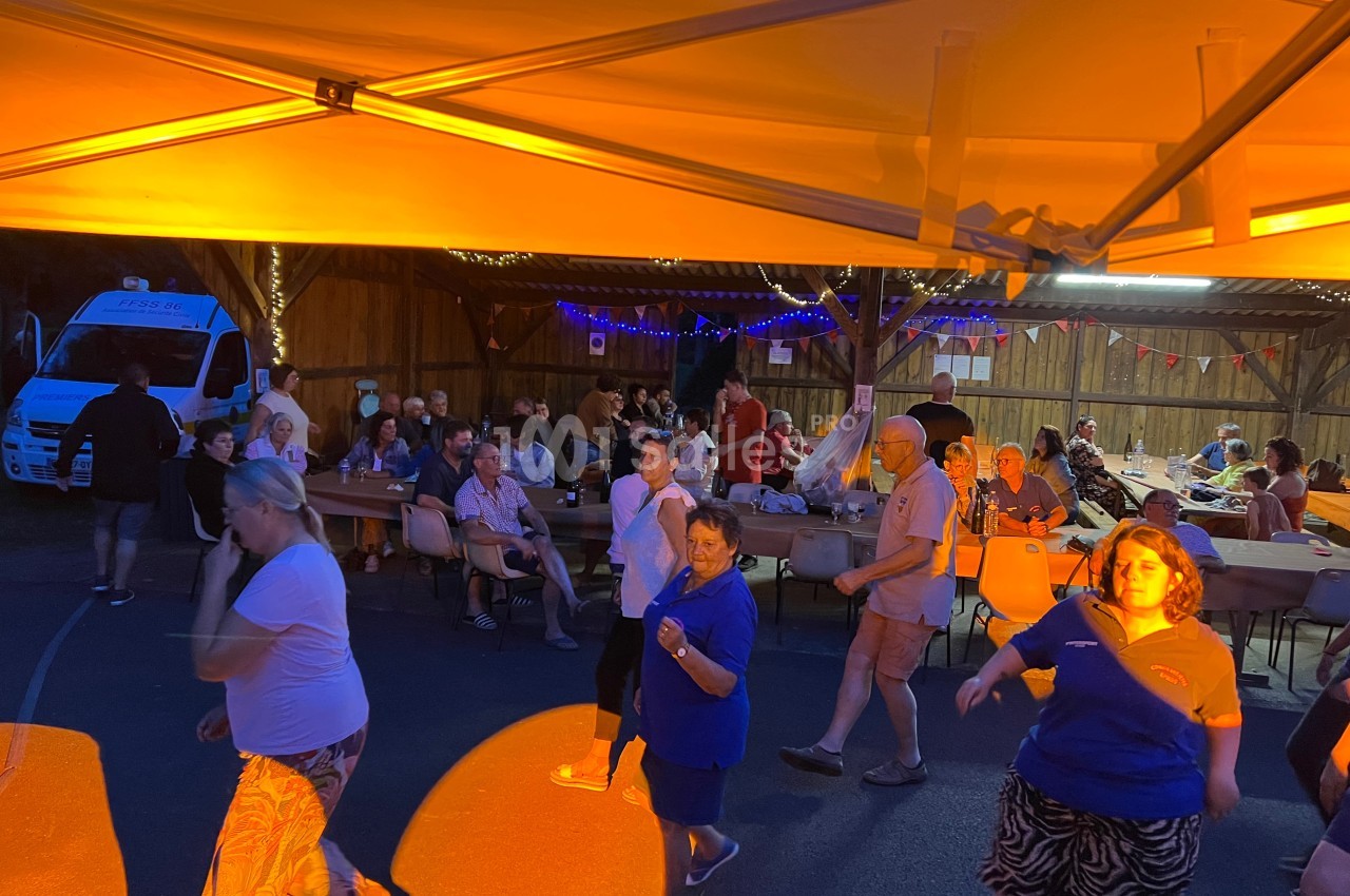Des personnes dansent et dînent sous un chapiteau éclairé en orange lors d'un événement en soirée.