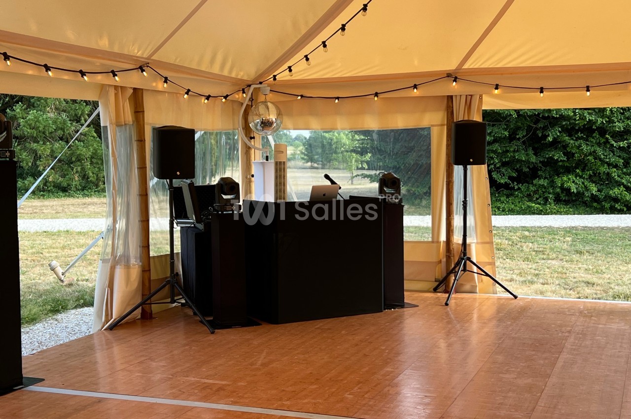 Piste de danse sous une tente avec une table de DJ, des enceintes, une boule disco et des guirlandes lumineuses.