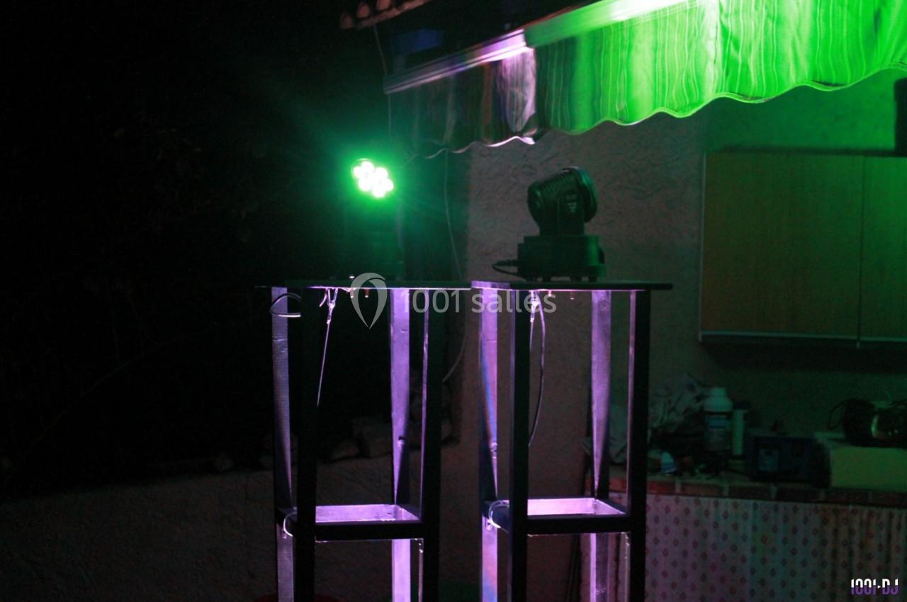 Deux projecteurs lumineux sur des supports métalliques éclairent une scène en extérieur, sous un auvent.