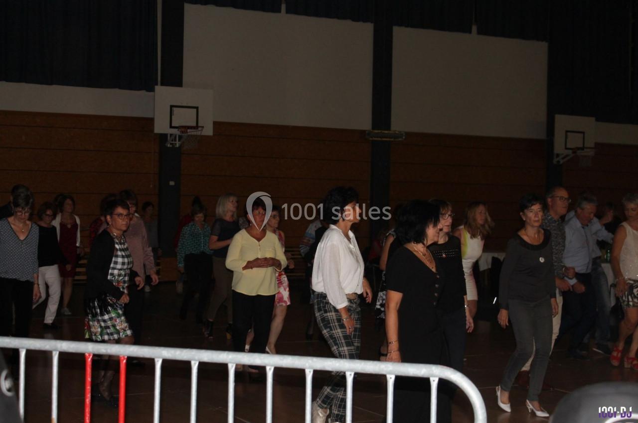 Des personnes participent à une séance de danse en groupe dans une salle de sport éclairée.