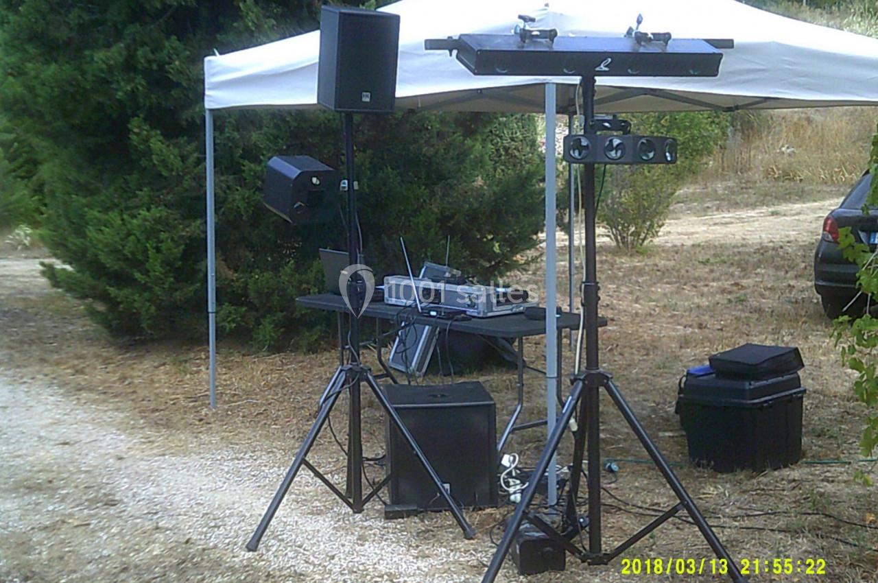 Équipement de sonorisation installé en extérieur sous une tente blanche, entouré de végétation.