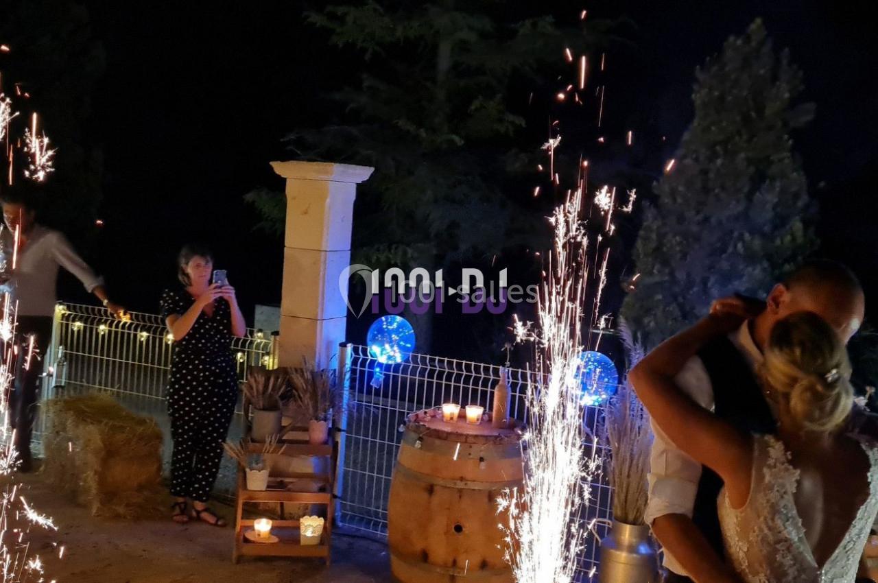 Un couple danse en soirée extérieure, entouré de décorations lumineuses et de gerbes d'étincelles.