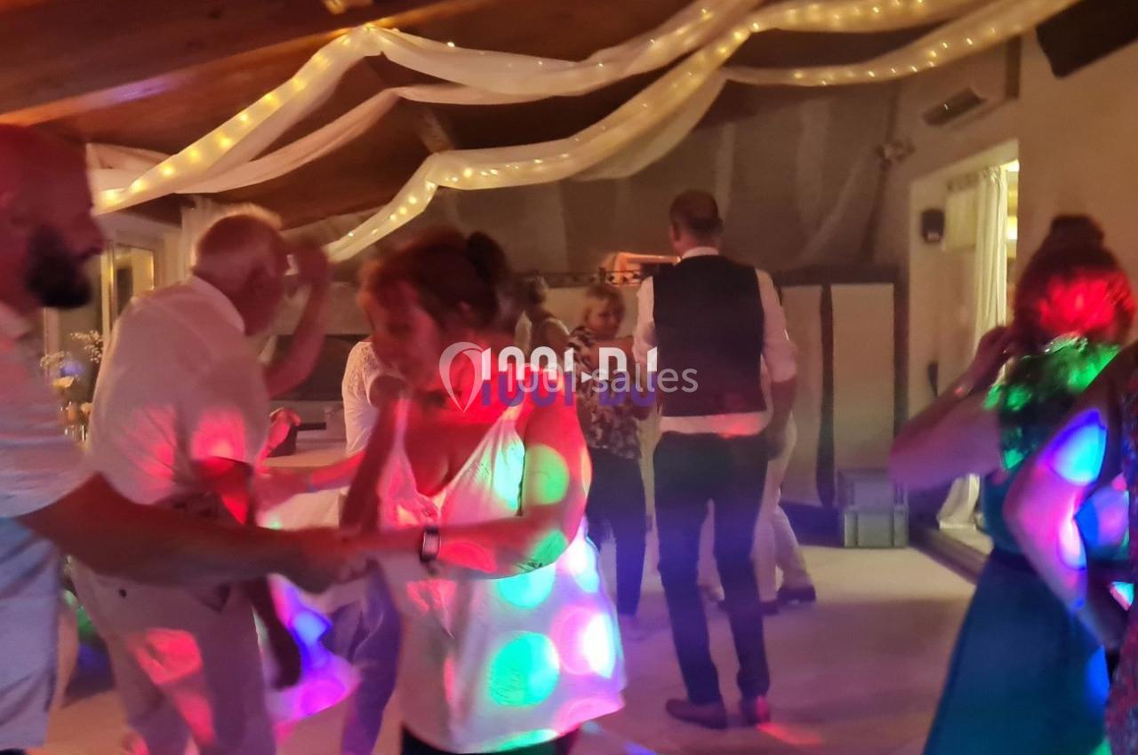 Des personnes dansent sous des lumières colorées dans une salle décorée de guirlandes et de voilages.