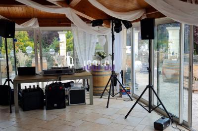 Équipement de sonorisation installé en extérieur sous une tente blanche, entouré de végétation.