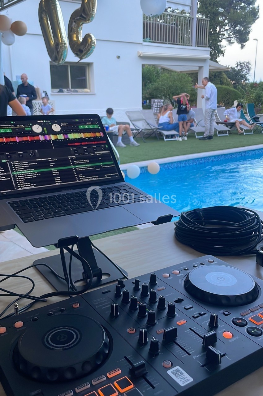 Table de mixage et ordinateur portable installés près d'une piscine lors d'une fête en extérieur.
