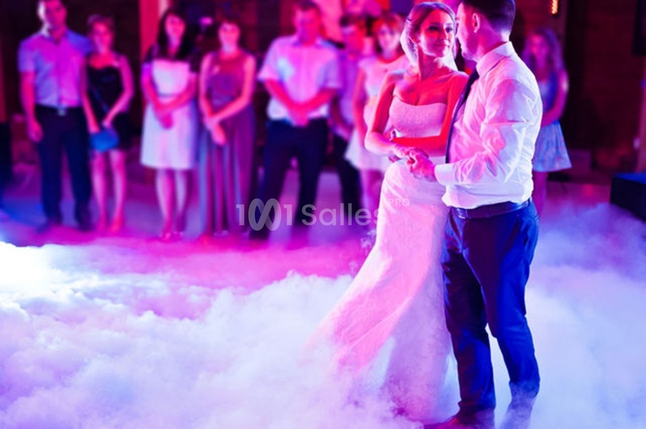 Un couple danse au milieu d'une piste entourée de fumée, avec des invités en arrière-plan.