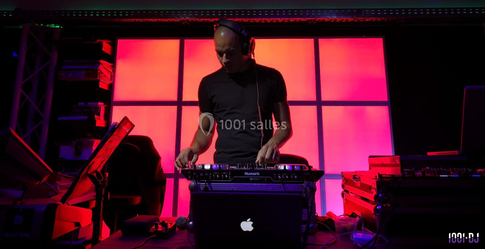Un DJ mixant de la musique sur une table de mixage, éclairé par des lumières rouges et violettes en arrière-plan.