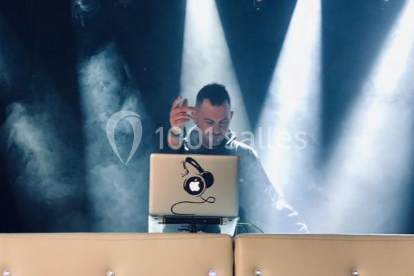 Un DJ mixe sur scène derrière un ordinateur portable, éclairé par des projecteurs dans une ambiance enfumée.