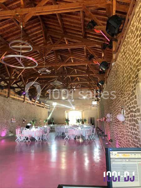 Salle de réception en pierre avec plafond en bois, tables décorées et éclairages colorés installés pour un événement.