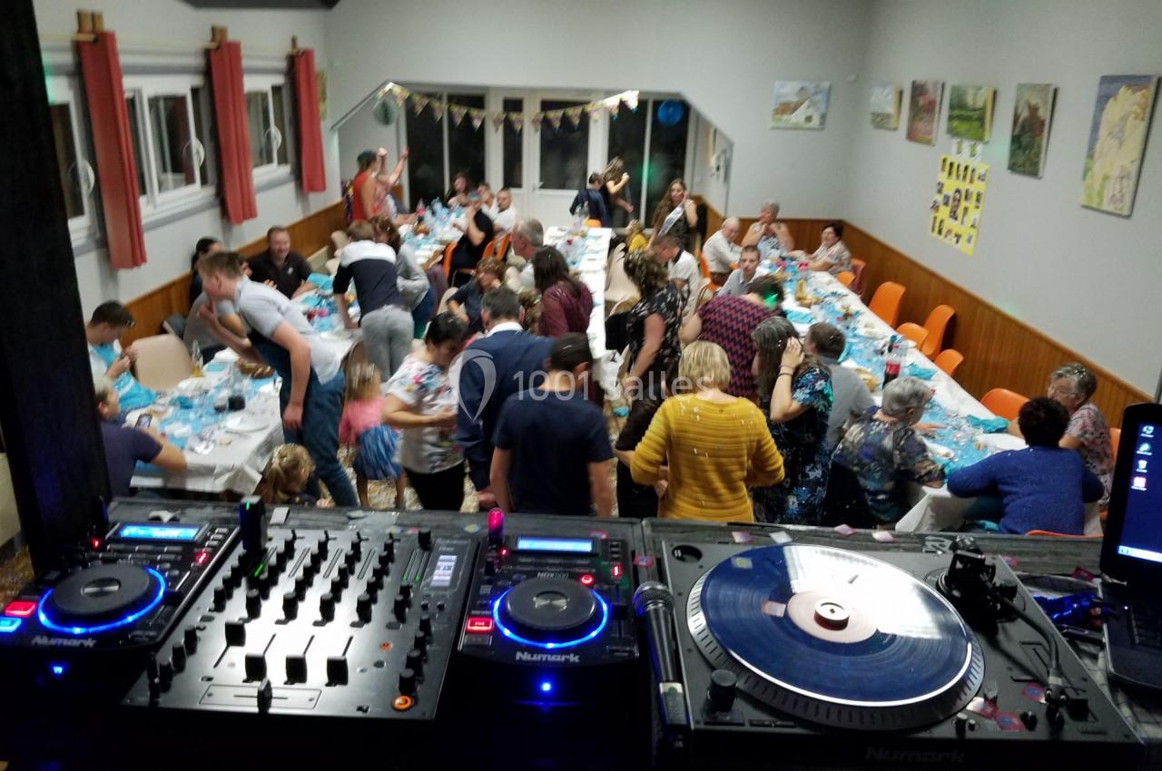 Salle animée avec des invités dînant à des tables décorées, vue depuis une table de mixage avec platine vinyle.