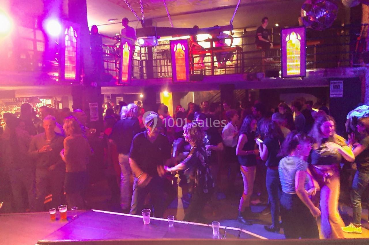 Personnes dansant et discutant dans une salle de fête animée avec éclairage coloré et mezzanine.