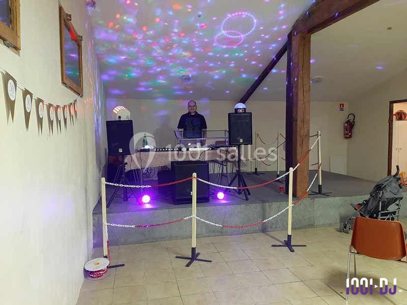Un DJ mixe sur une scène éclairée par des jeux de lumière colorés dans une salle décorée pour un événement.