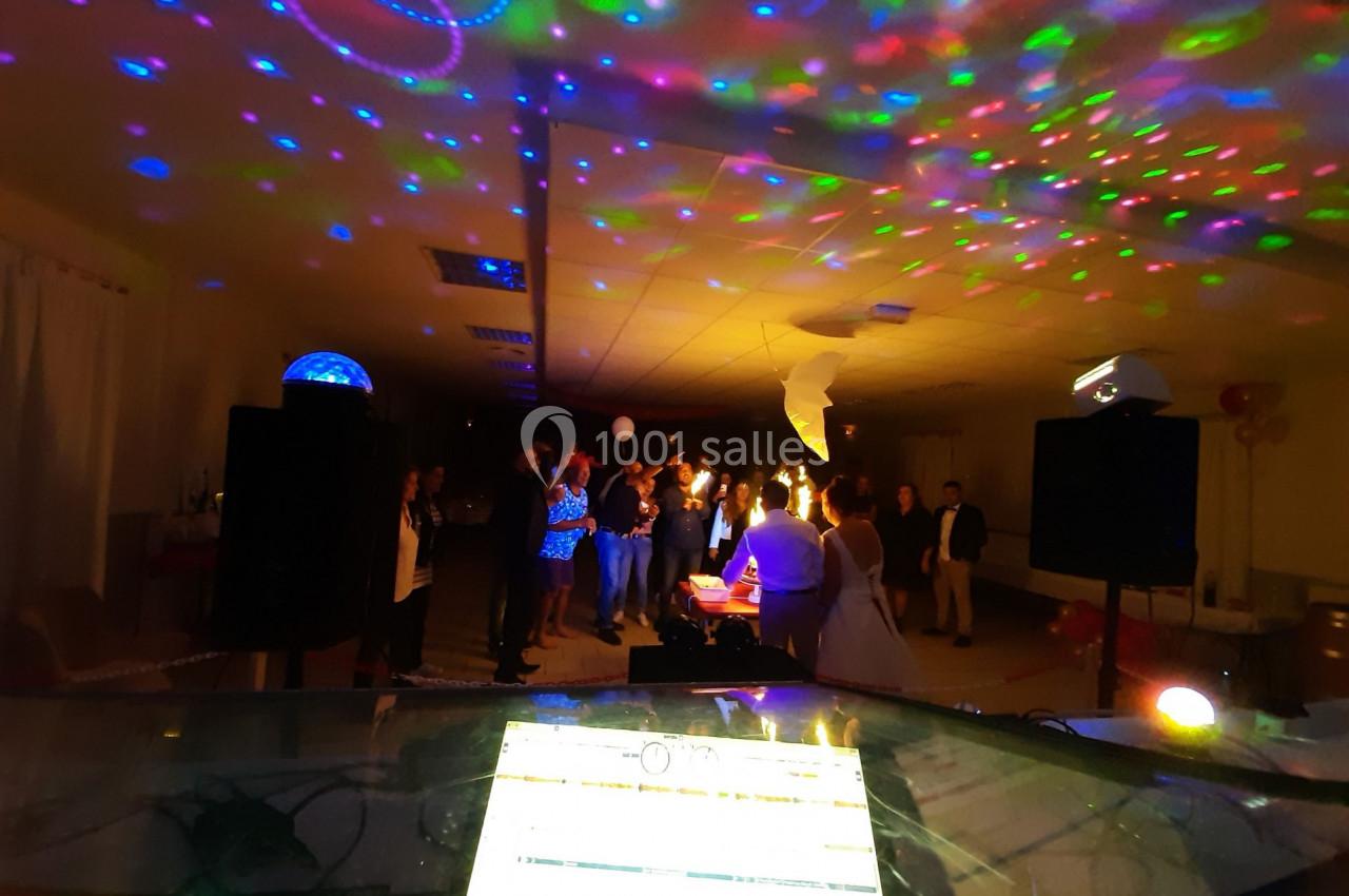 Vue d'une salle de fête avec des invités dansant sous des lumières colorées et un DJ en arrière-plan.