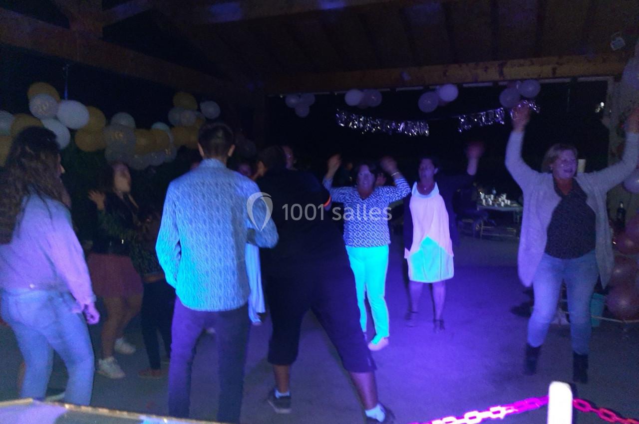 Des personnes dansent sous un abri décoré de ballons et guirlandes lumineuses, dans une ambiance festive nocturne.