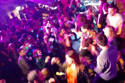 Des personnes dansent sous un abri décoré de ballons et guirlandes lumineuses, dans une ambiance festive nocturne.