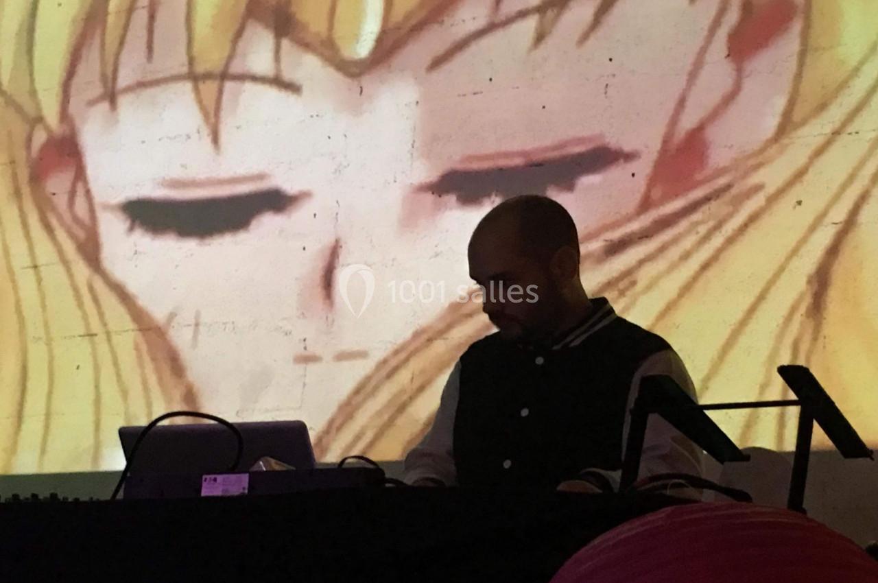 Un DJ mixe devant une projection murale d'un personnage d'animation aux yeux fermés.