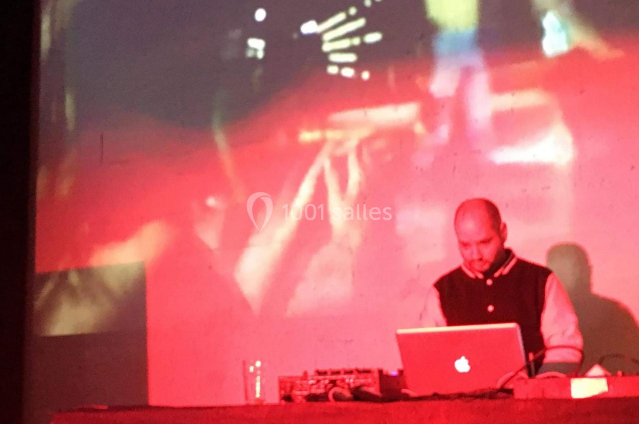 Un homme utilise un ordinateur portable sur une table, éclairé par une lumière rouge avec un écran projeté en arrière-plan.