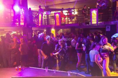 Des personnes dansent sous un abri décoré de ballons et guirlandes lumineuses, dans une ambiance festive nocturne.