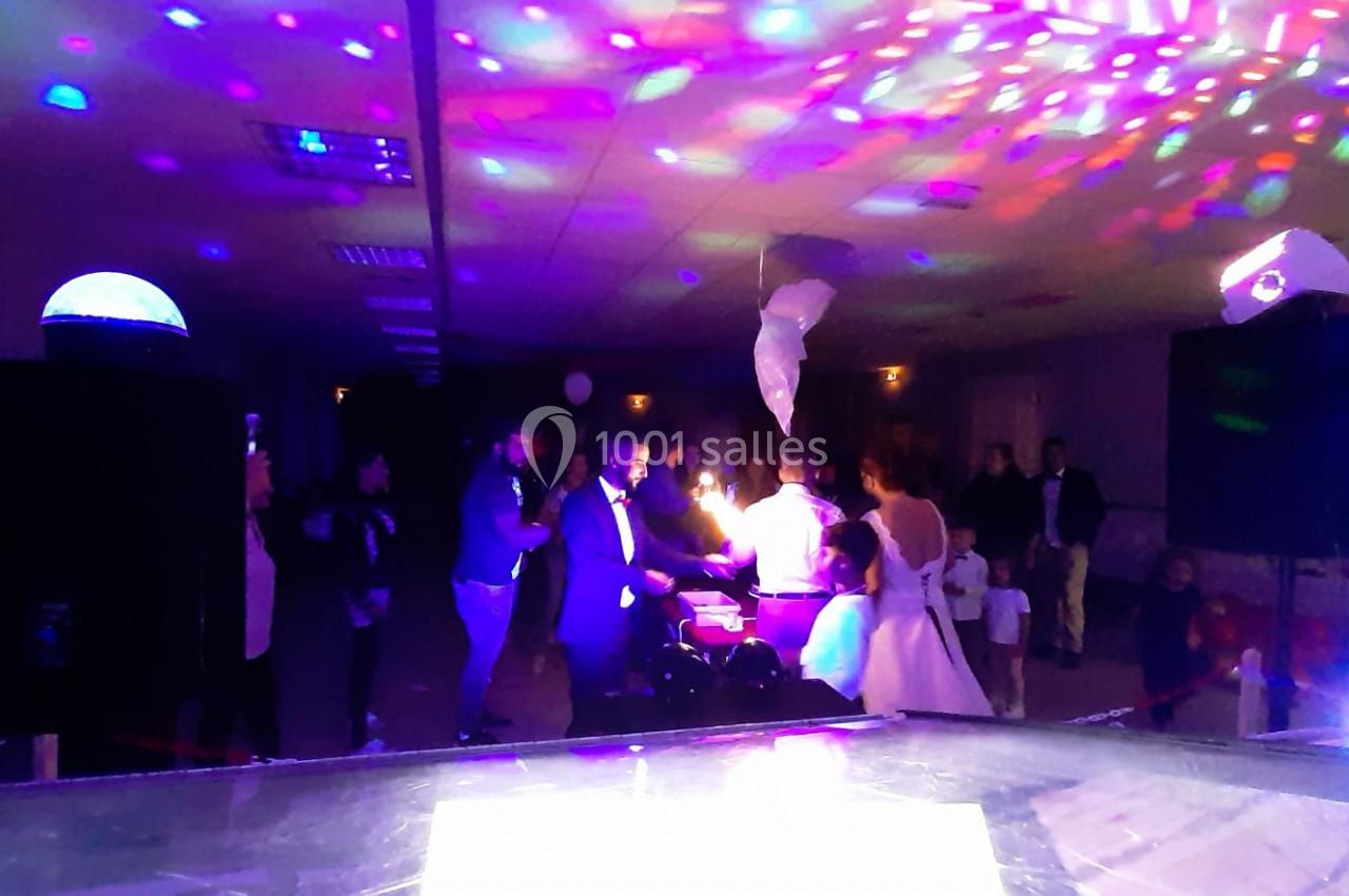 Des invités dansent dans une salle éclairée par des lumières colorées lors d'une fête ou d'un événement festif.