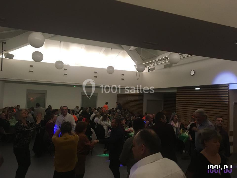 Des personnes dansent et discutent dans une salle de réception éclairée, avec des tables occupées en arrière-plan.