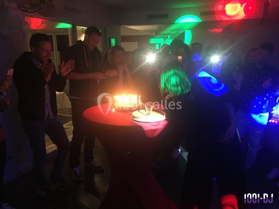Des personnes réunies autour d'un gâteau d'anniversaire illuminé par des bougies dans une ambiance festive.