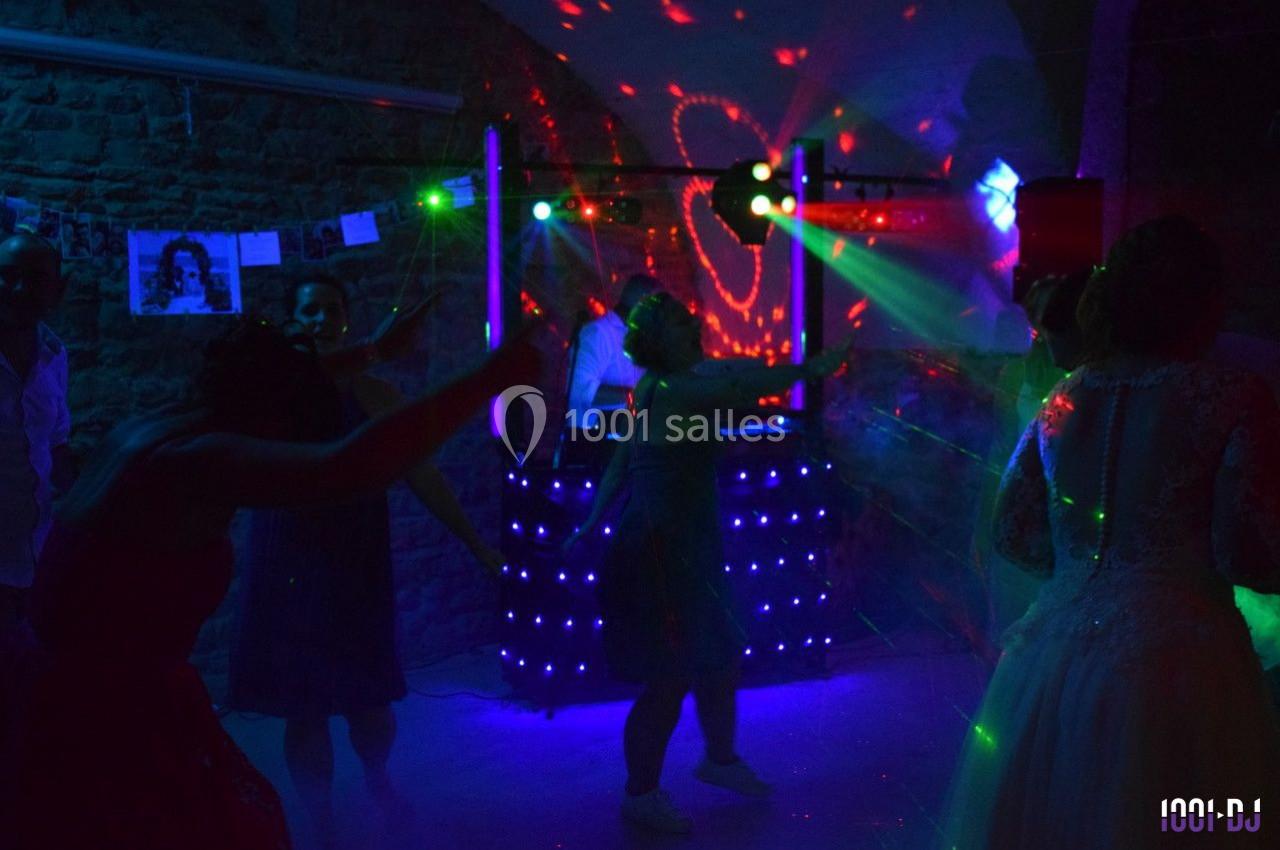 Personnes dansant sous des lumières colorées lors d'une soirée animée par un DJ dans une salle en pierre.