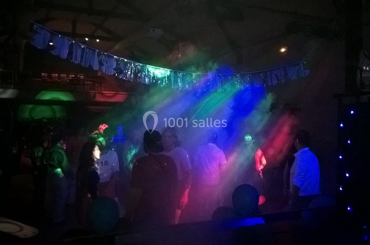 Personnes dansant sous des lumières colorées et des effets de fumée dans une salle sombre décorée pour une fête.