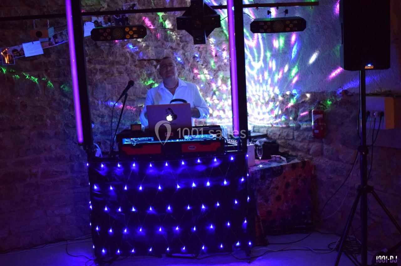 Un DJ mixe derrière une table éclairée par des lumières LED colorées dans une salle en pierre.