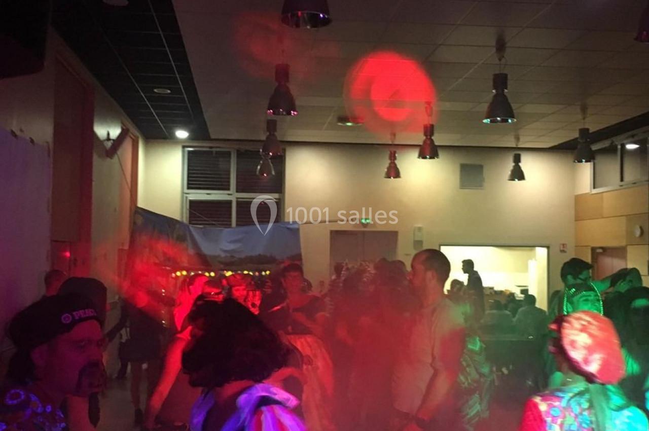 Personnes déguisées dansant dans une salle éclairée par des lumières colorées lors d'une fête.