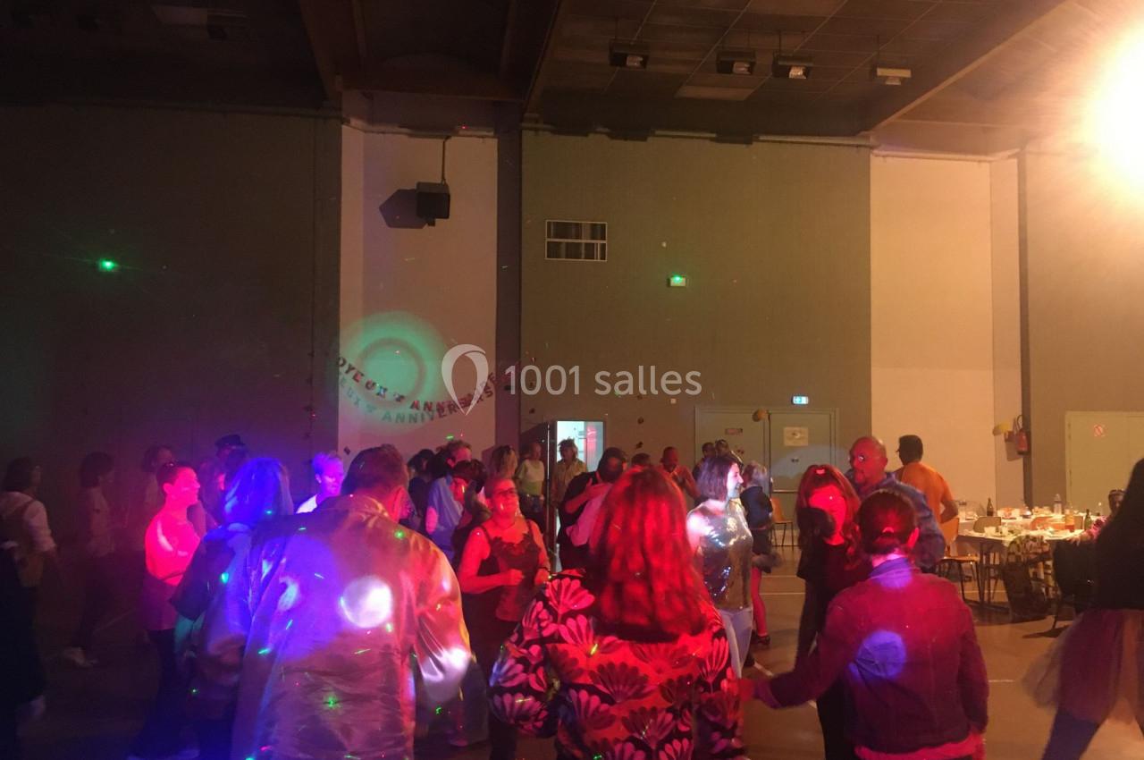 Des personnes dansent dans une salle éclairée par des lumières colorées lors d'un événement festif.