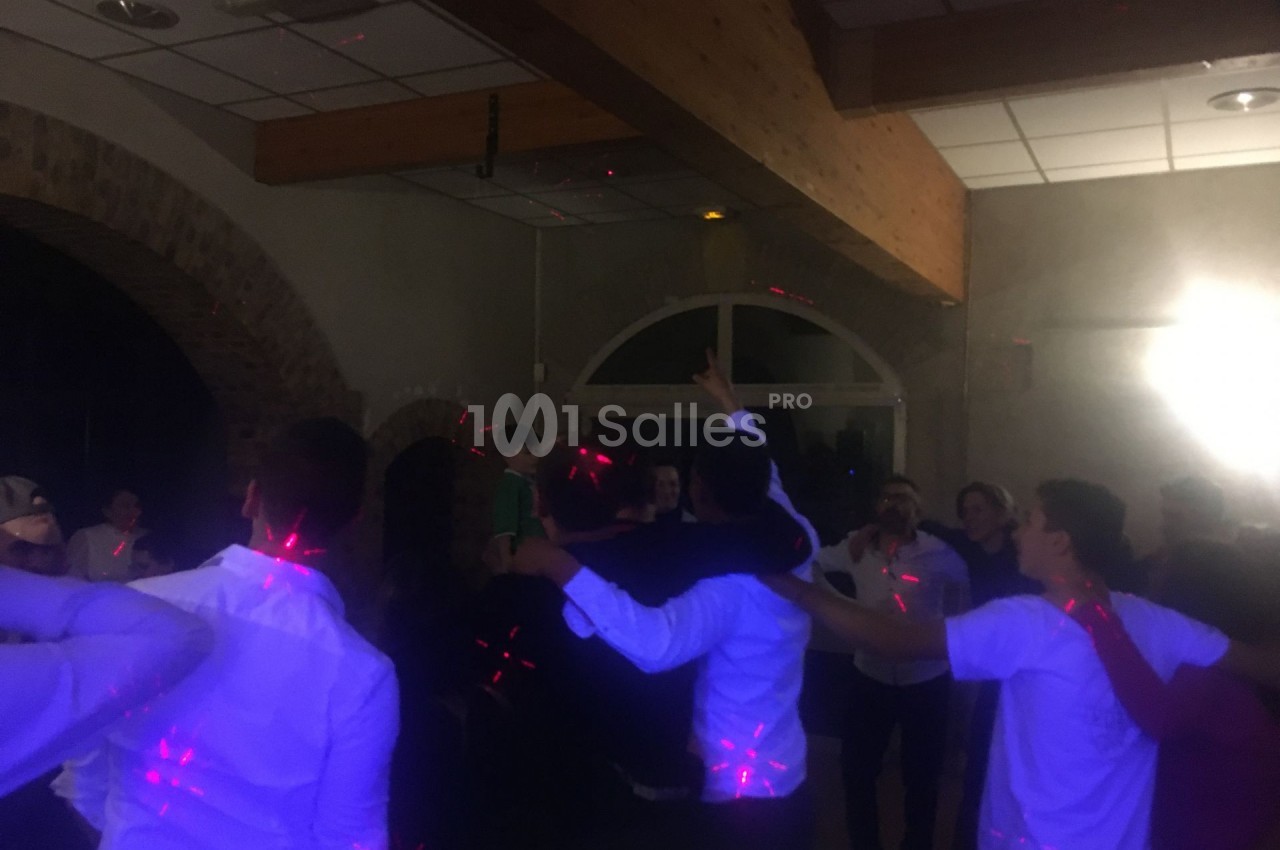 Groupe de personnes dansant sous des lumières colorées dans une salle avec des murs en pierre et un plafond en bois.