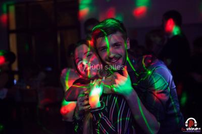 Des personnes dansent en ligne dans une salle décorée de ballons, avec des tables dressées et des convives en arrière-plan.