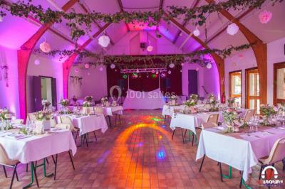 Des personnes dansent en ligne dans une salle décorée de ballons, avec des tables dressées et des convives en arrière-plan.