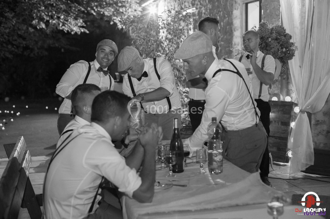 Des hommes en tenue rétro discutent et rient autour d'une table lors d'un événement en extérieur, éclairé par des lumières…