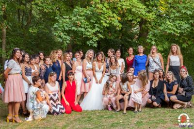 Des personnes dansent en ligne dans une salle décorée de ballons, avec des tables dressées et des convives en arrière-plan.